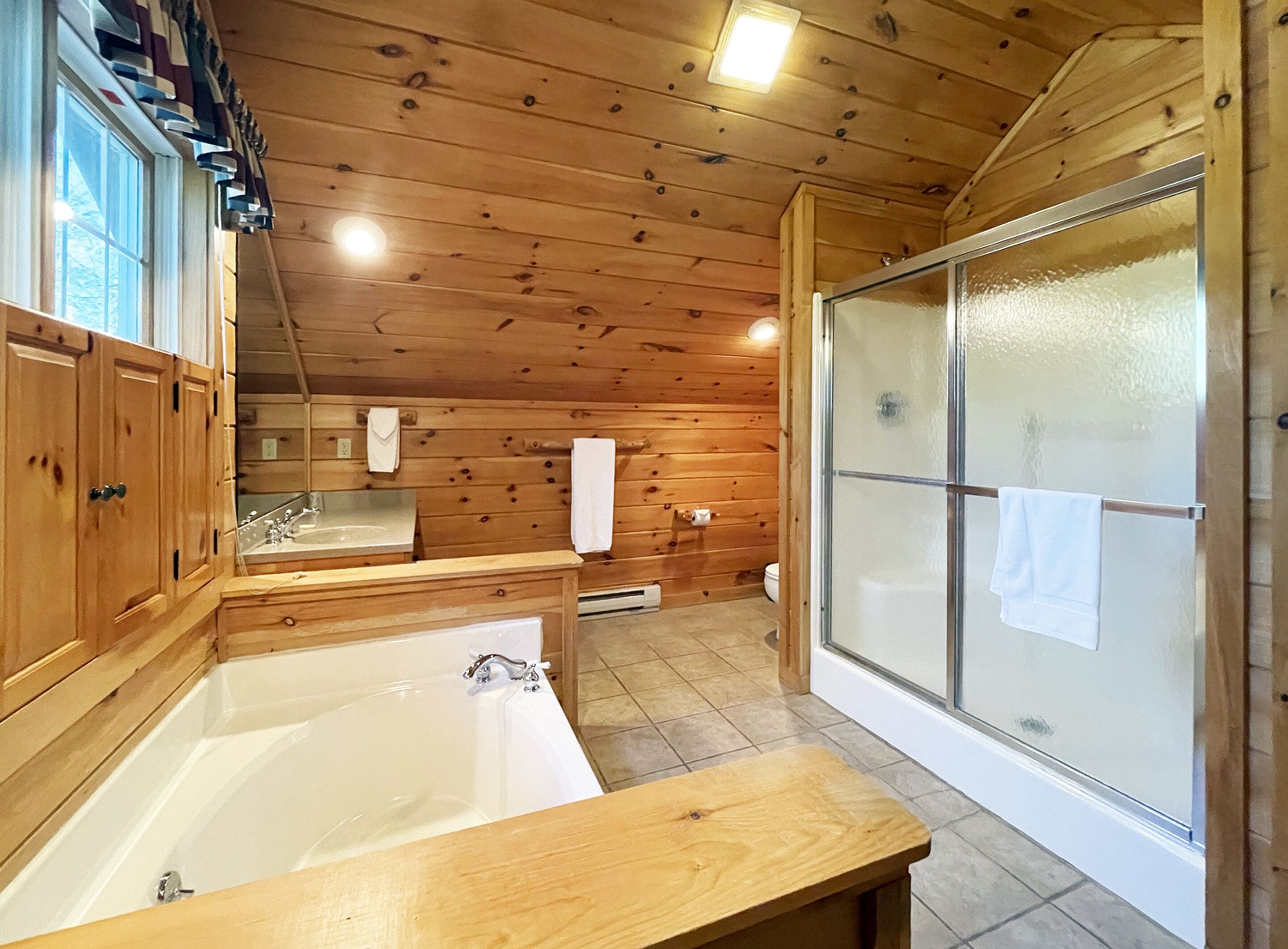 A wooden cabin bathroom with a bathtub, a sink, and a shower area.