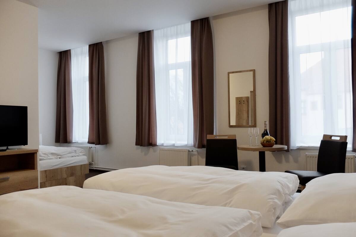Habitación de hotel con dos camas, un televisor, una mesa con una botella y vasos, y un espejo en la pared.