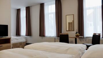 A hotel room with two beds, a television, a table with a bottle and glasses, and a mirror on the wall.