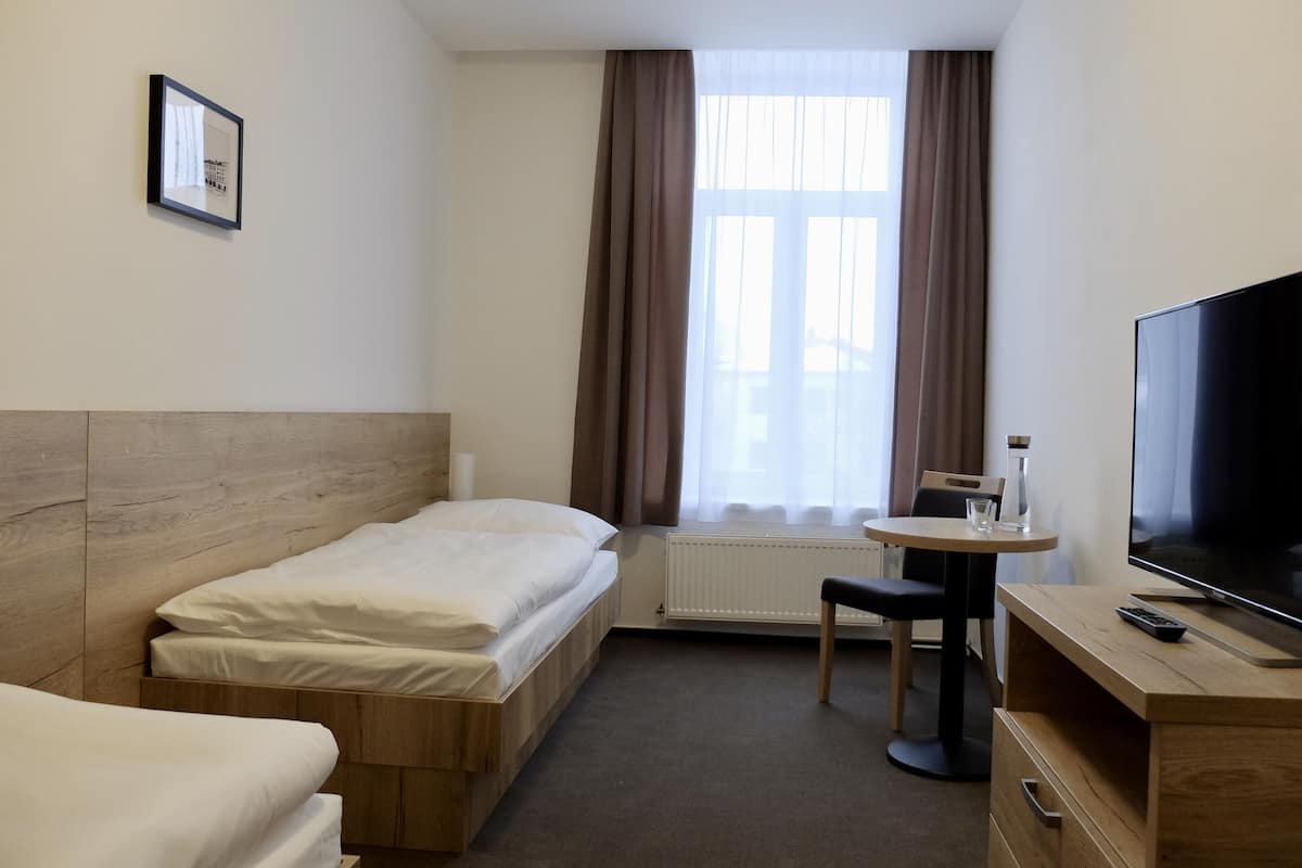 Una habitación de hotel con cama, escritorio, silla, televisión y ventana con cortinas.