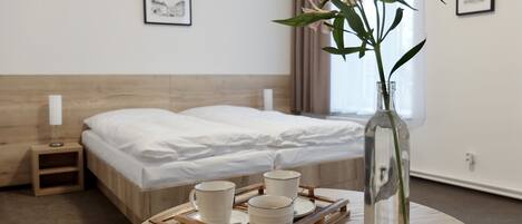 A hotel room with a bed, a bedside table with a lamp, a tray with cookies and cups, and a vase with flowers.