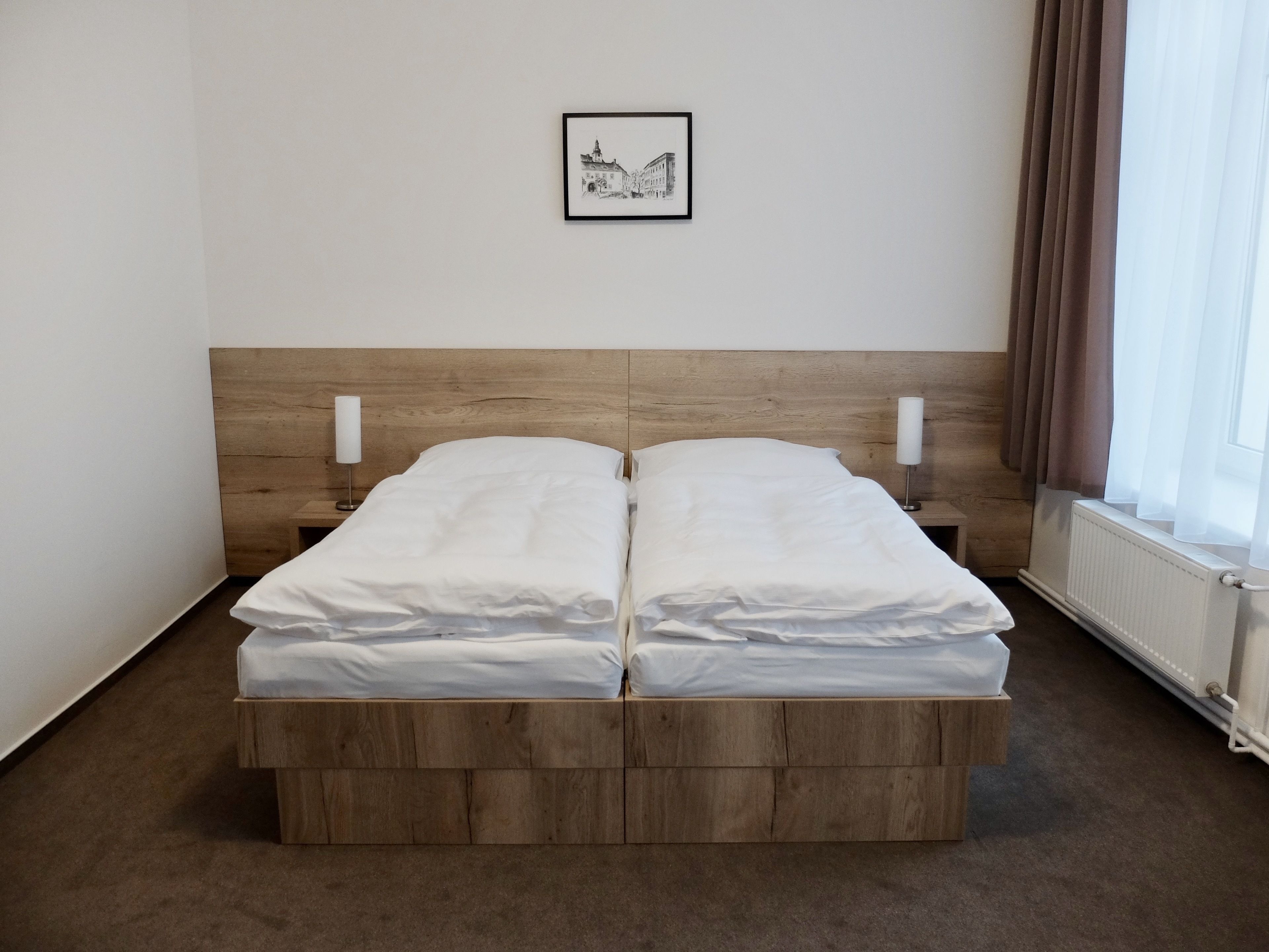 Een tweepersoonsbed met een houten hoofdbord, witte beddengoed en twee nachtkastjes met lampen.