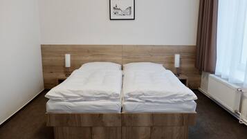 Een tweepersoonsbed met een houten hoofdbord, witte beddengoed en twee nachtkastjes met lampen.