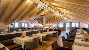 A spacious dining area with wooden beams, multiple tables, and chairs.