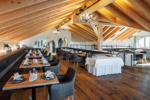 A restaurant with wooden beams, tables set for dining, and a staircase leading to an upper level. - Bergresort Das JOCHELIUS (Nauders)