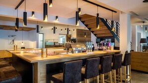 A modern bar area with a long counter, multiple hanging pendant lights, and bar stools.