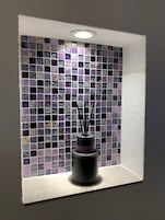 Pared con un diseño de mosaicos y un florero negro con ramas.