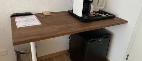Una kitchenette compacta con cafetera, refrigerador pequeño y un basurero.