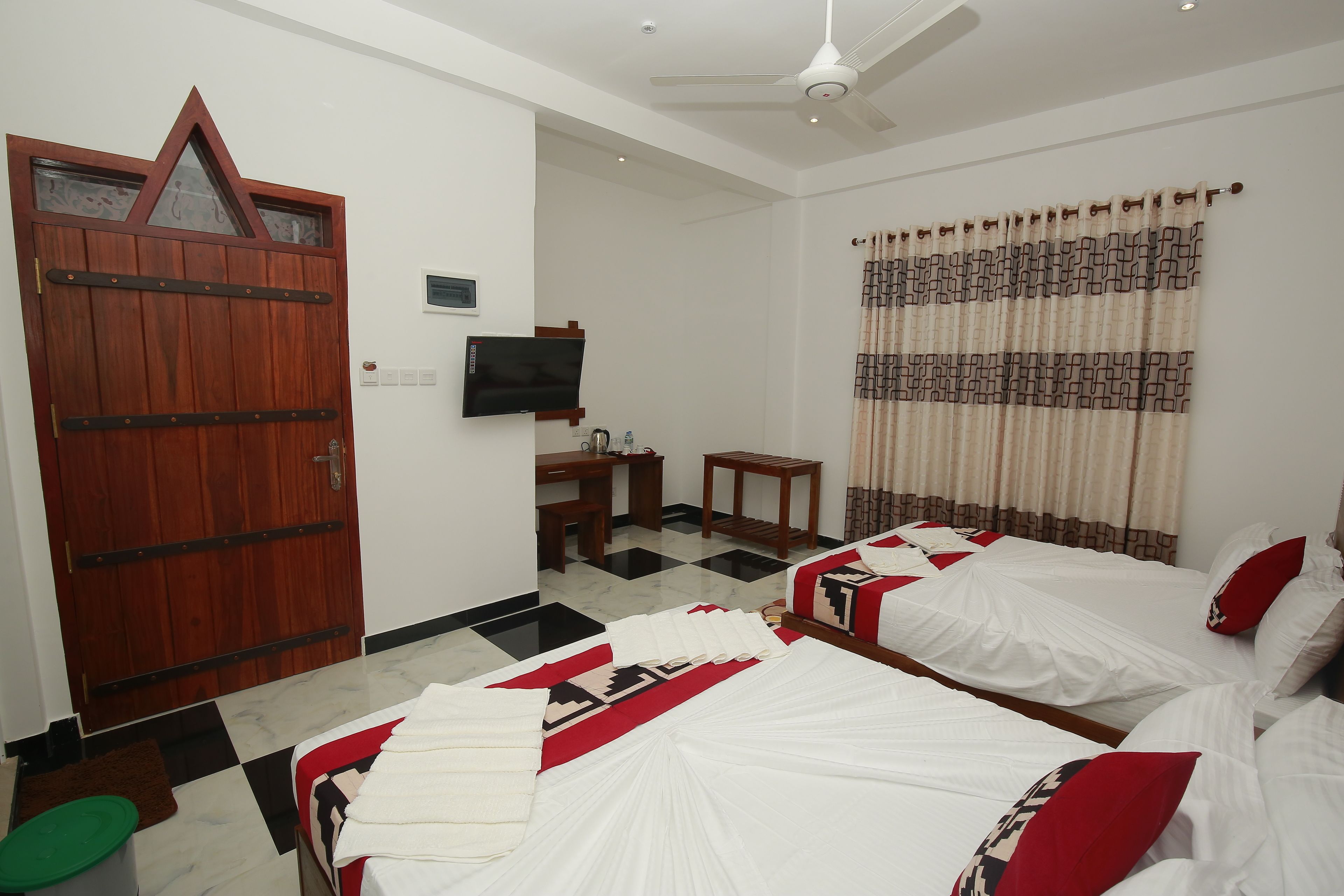 Habitación de hotel con dos camas, una puerta de madera, un televisor, un escritorio y un ventilador de techo.