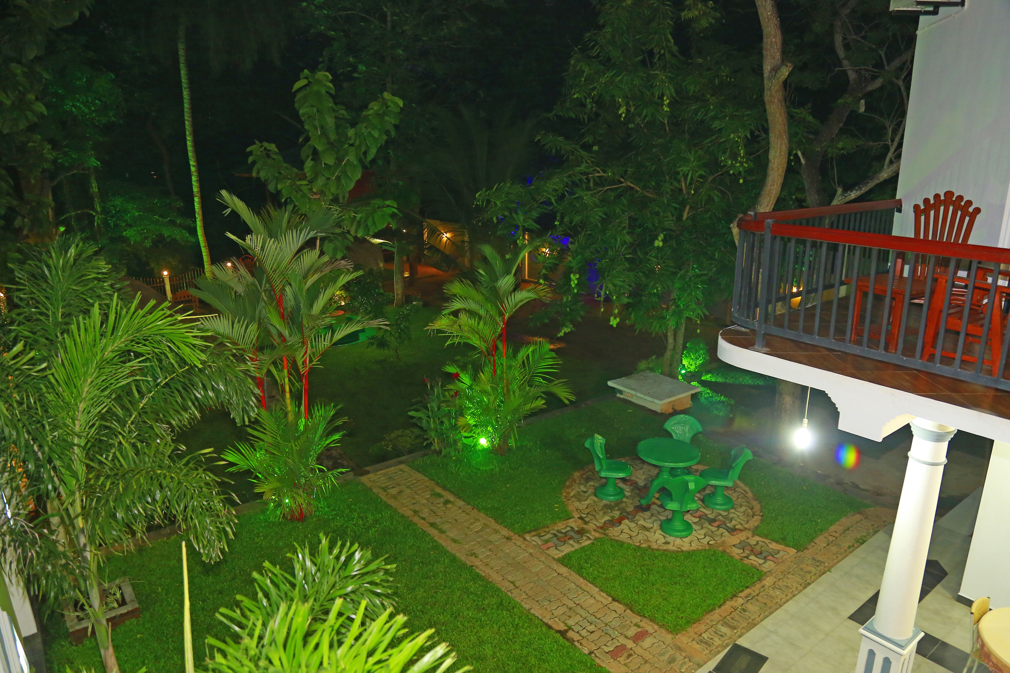 Un jardín con un patio empedrado, sillas verdes y una pequeña mesa.