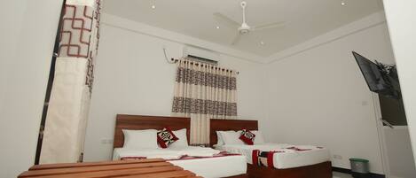 A hotel room with two beds, a ceiling fan, an air conditioning unit, a TV mounted on the wall, and a wooden bench.