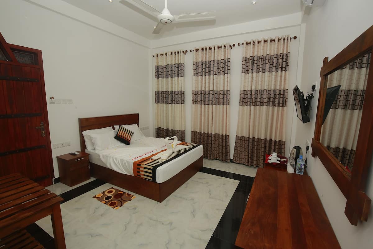 A bedroom with a bed, wooden furniture, a ceiling fan, curtains, and a small table.