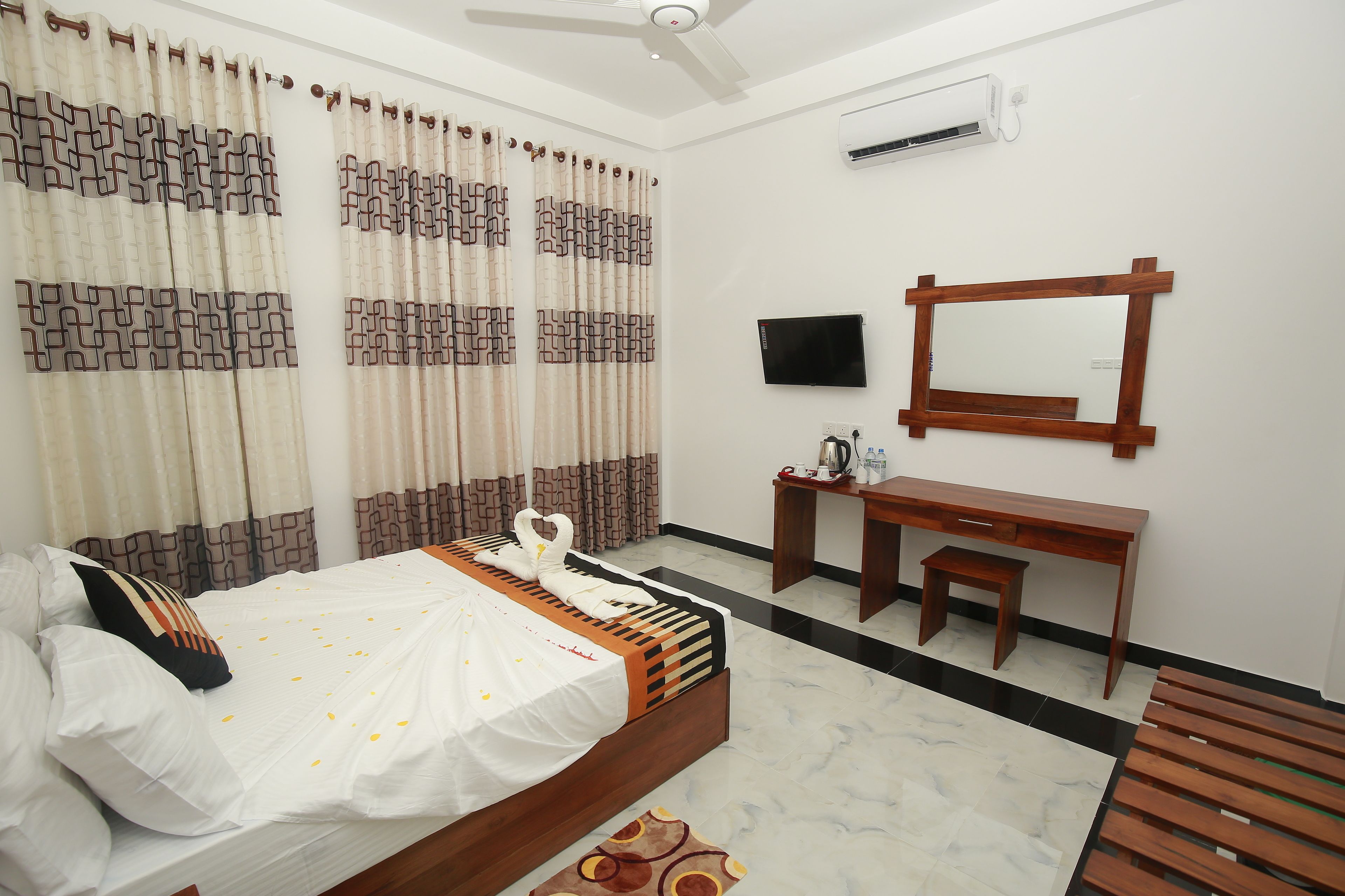 Quarto de hotel com cama, escrivaninha, cadeira, televisão e ar condicionado.