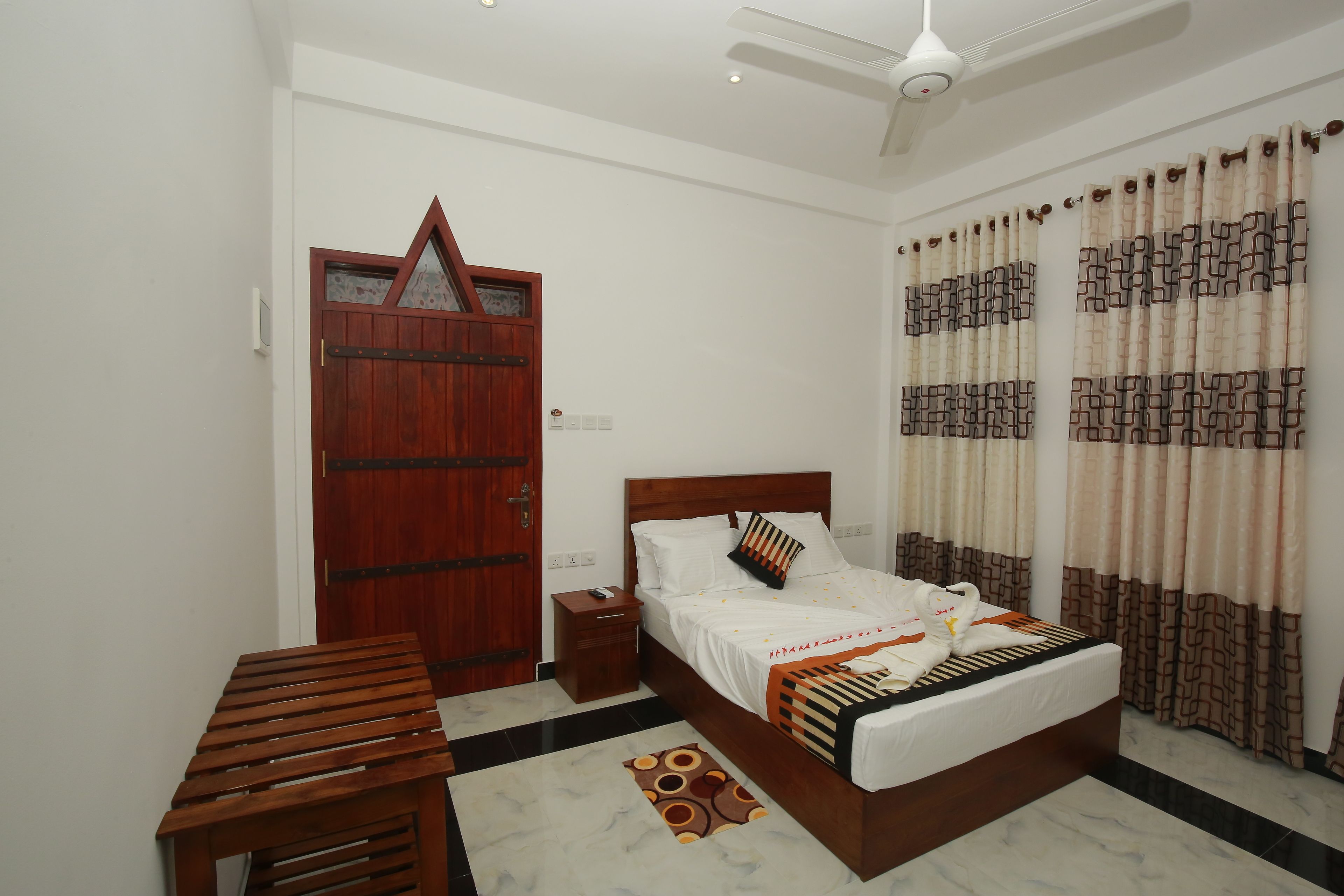 Un dormitorio con una cama de madera, una mesita de noche, una mesa de madera, un tapete estampado y una puerta decorativa.