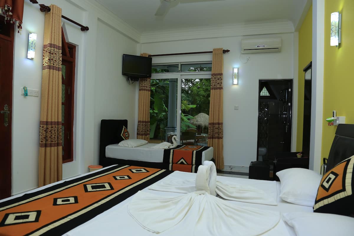 A hotel room with a bed, a television, a window with curtains, and a view of greenery outside.