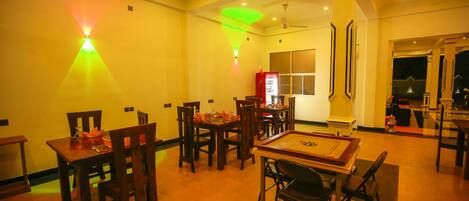 A dining area with wooden tables and chairs, a ceiling fan, and a vending machine.