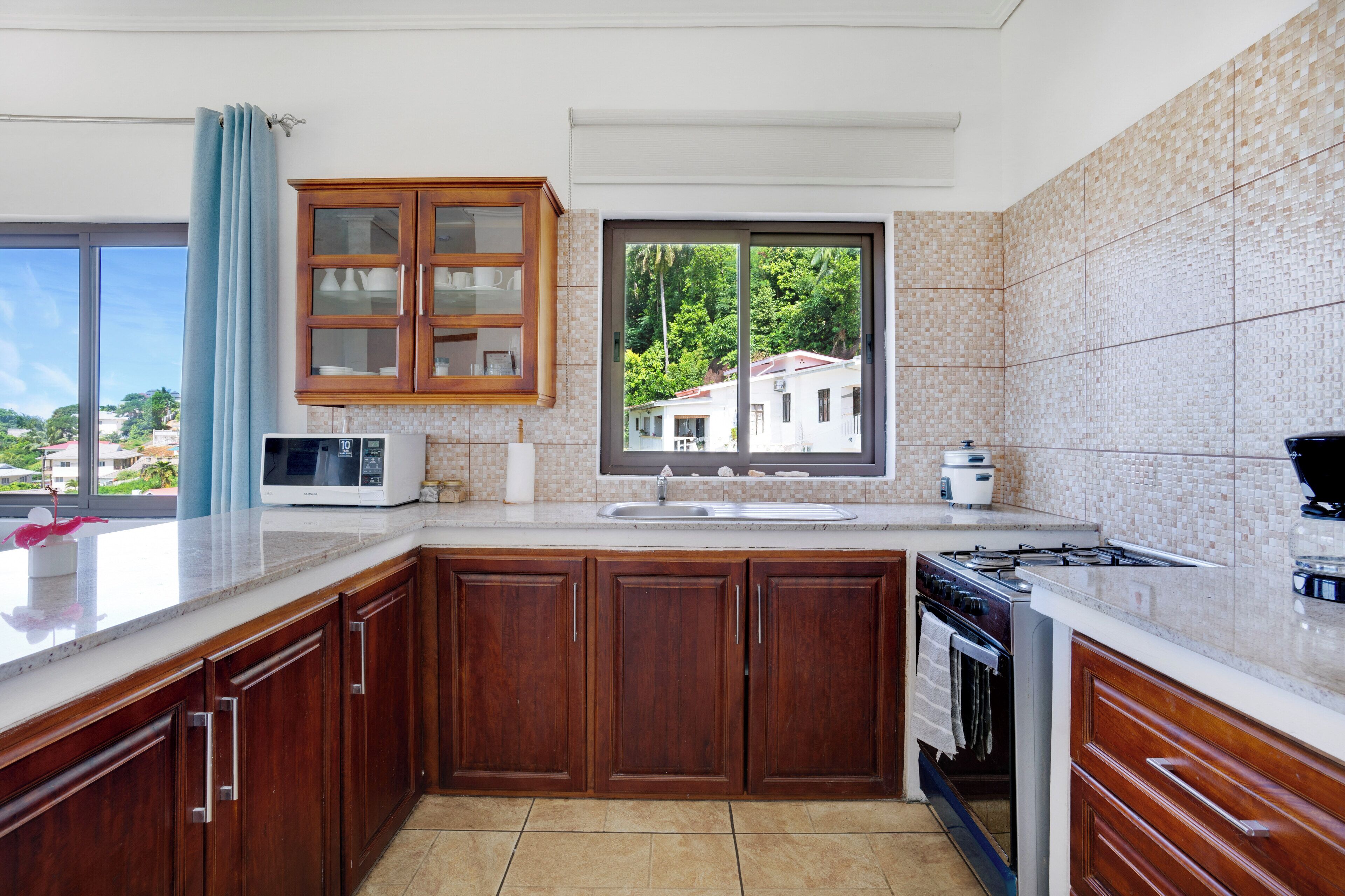 A kitchen with wooden cabinets, a microwave, a stove, and a window with a view of houses.