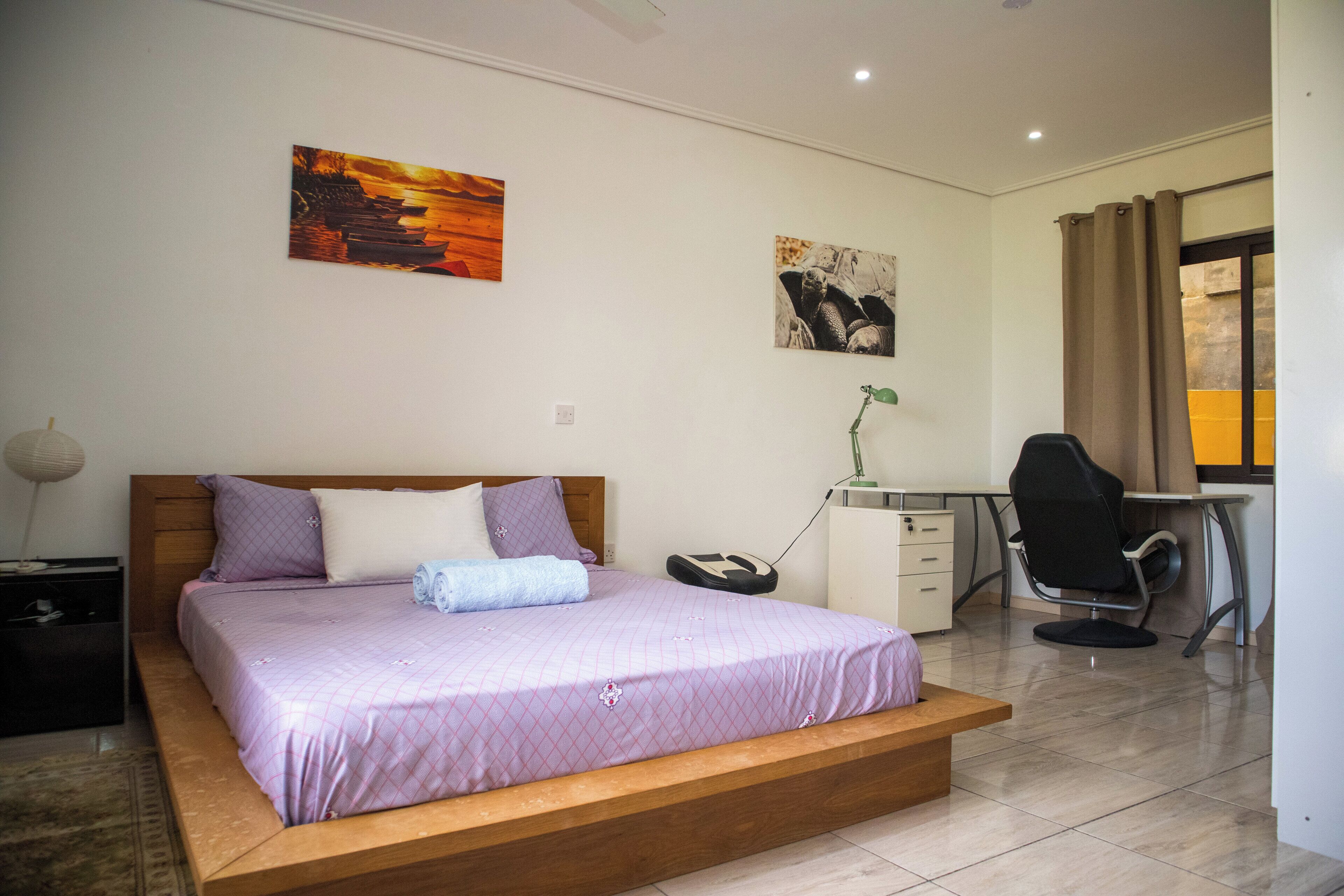 Een slaapkamer met een bed, bureau, stoel en kunstwerken aan de wanden.