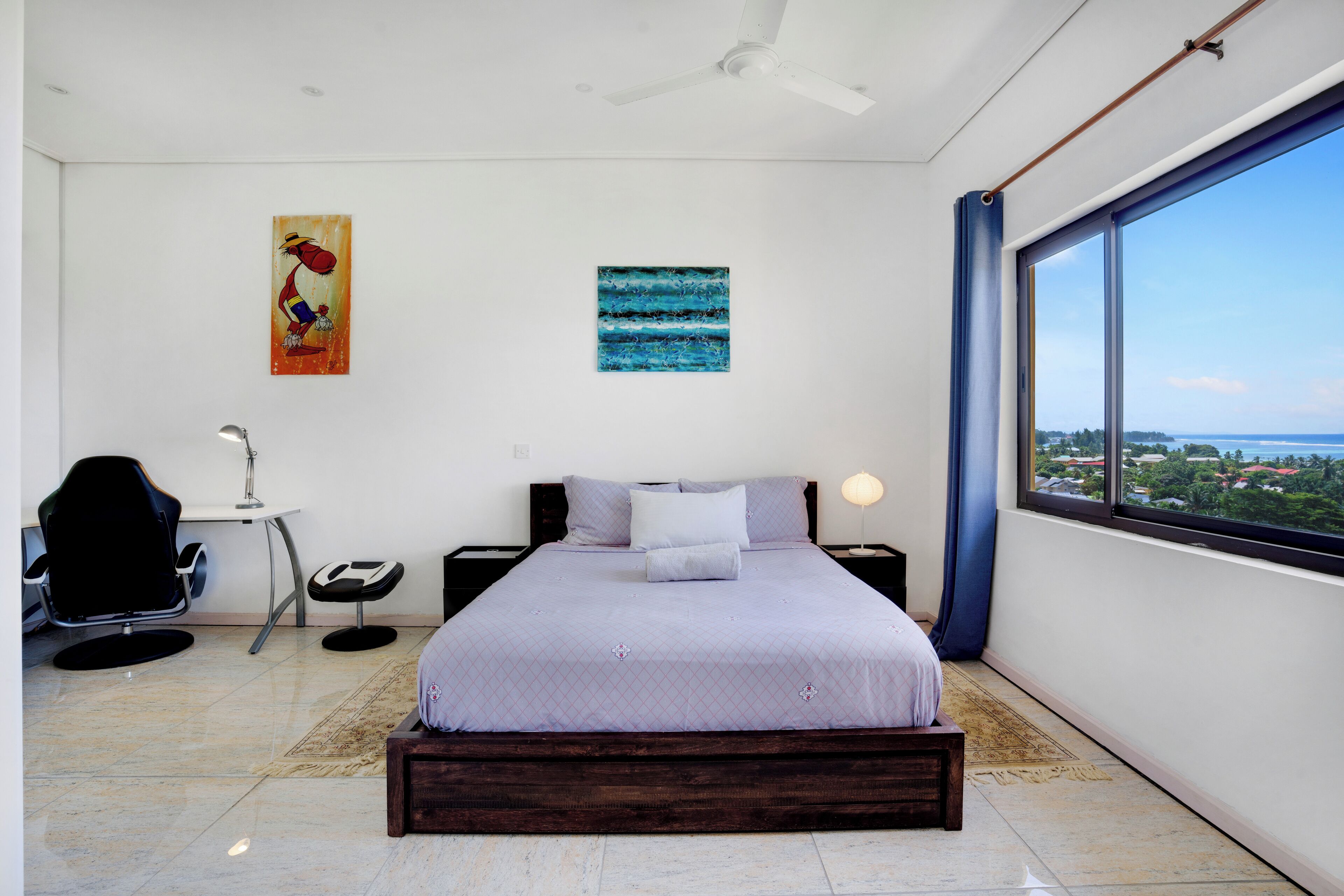Une chambre moderne avec un grand lit, un bureau, une chaise et une vue sur la ville grâce à une grande fenêtre.