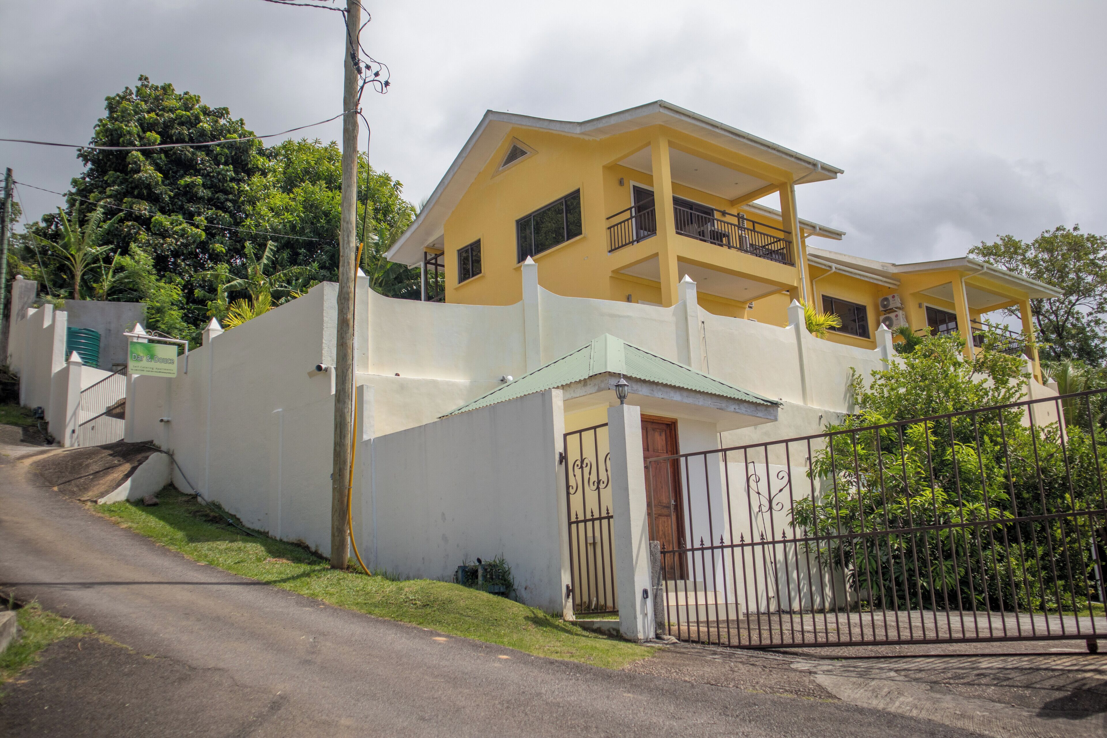 A two-story building with a balcony on the upper floor, a gated entrance, and a white fence surrounding the property.