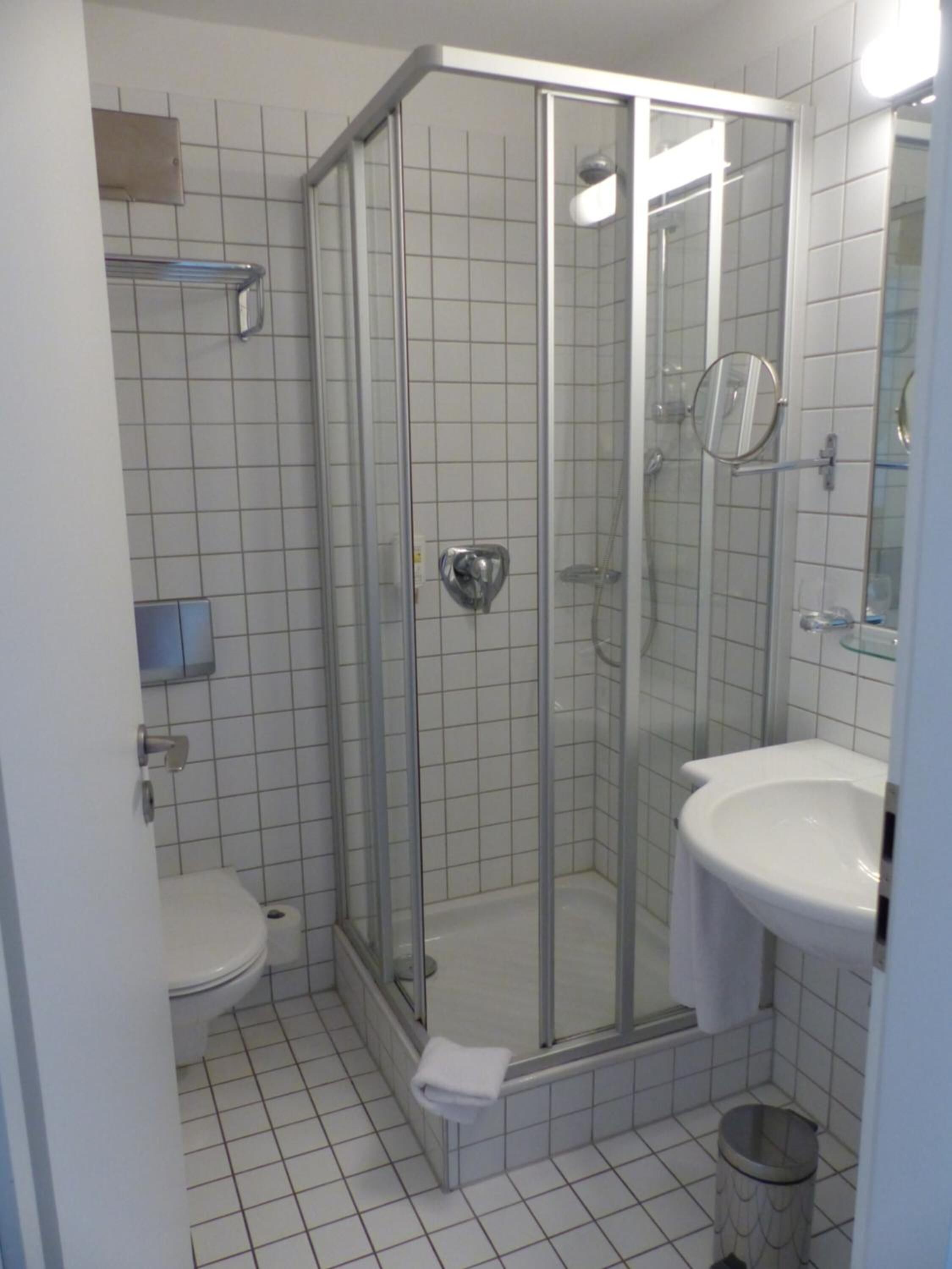 Une petite salle de bain carrelée, dotée d’une douche à parois de verre, de toilettes et d’un lavabo.