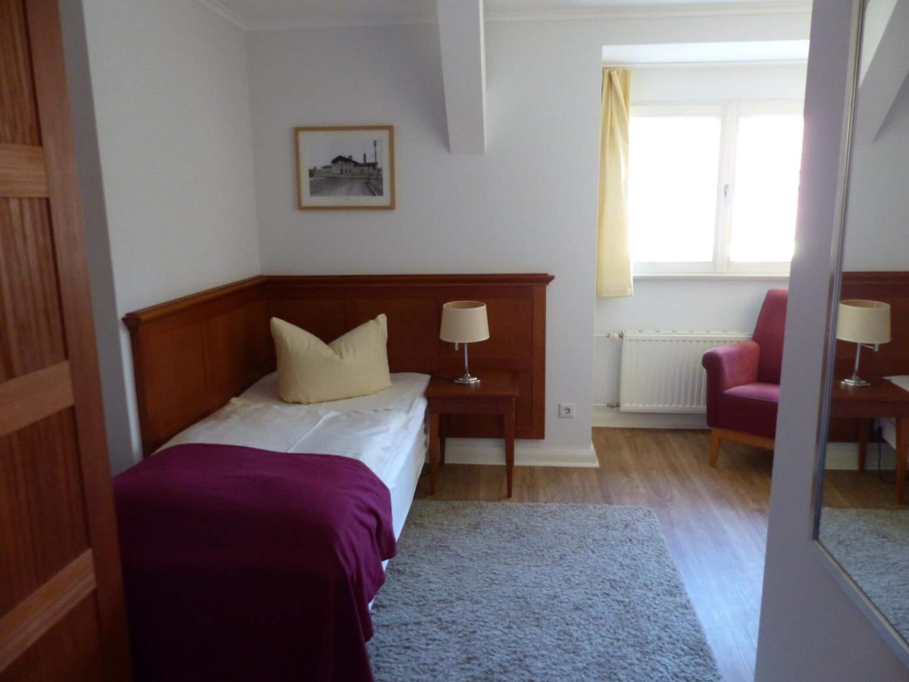 Un dormitorio con cama doble, una mesita de noche con lámpara, una silla y una ventana con cortinas.