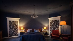 A bedroom with a large bed, two nightstands, a red armchair, a floor lamp, and a chandelier. - Hotel Vierseithof Luckenwalde (Luckenwalde)