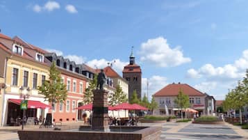 A public square with a central statue, surrounding buildings, and a clear sky.