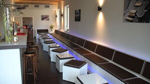 A modern bar area with a long counter, stools, and a seating area with a tiled bench. - Hotel Vierseithof Luckenwalde (Luckenwalde)
