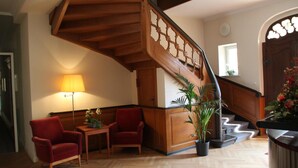 A spacious living area with a wooden staircase, two red armchairs, a small table, and a floor lamp. - Hotel Vierseithof Luckenwalde (Luckenwalde)