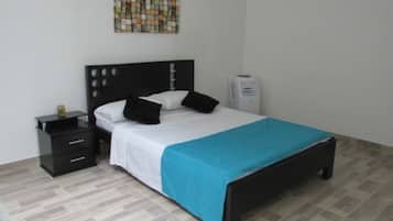 Un dormitorio ordenado con cama, mesita de noche, calefactor y una obra de arte en la pared.