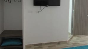 A room with a mounted TV on the wall, a wooden bench with cushions, and a door leading to another room. - SGreen Duplex Apartments I (Cali)