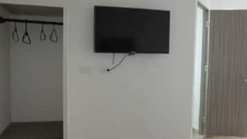 Una habitación con un televisor montado en la pared, un banco de madera con cojines y una puerta que da a otra estancia.