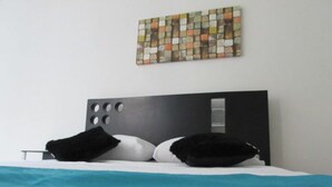A modern hotel room with a bed, a headboard with circular cutouts, and a colorful abstract artwork on the wall. - SGreen Duplex Apartments I (Cali)