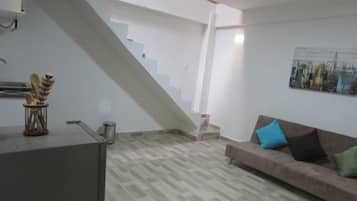 Una sala de estar moderna con una escalera, un sofá con cojines y un cuadro de un paisaje urbano en la pared.