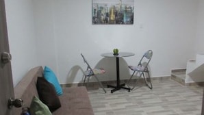 A small, furnished room with a brown sofa, a round table, two chairs, and a cityscape painting on the wall. - SGreen Duplex Apartments I (Cali)