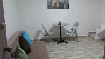 Una habitación pequeña y amoblada con un sofá marrón, una mesa redonda, dos sillas y un cuadro de un paisaje urbano en la pared.