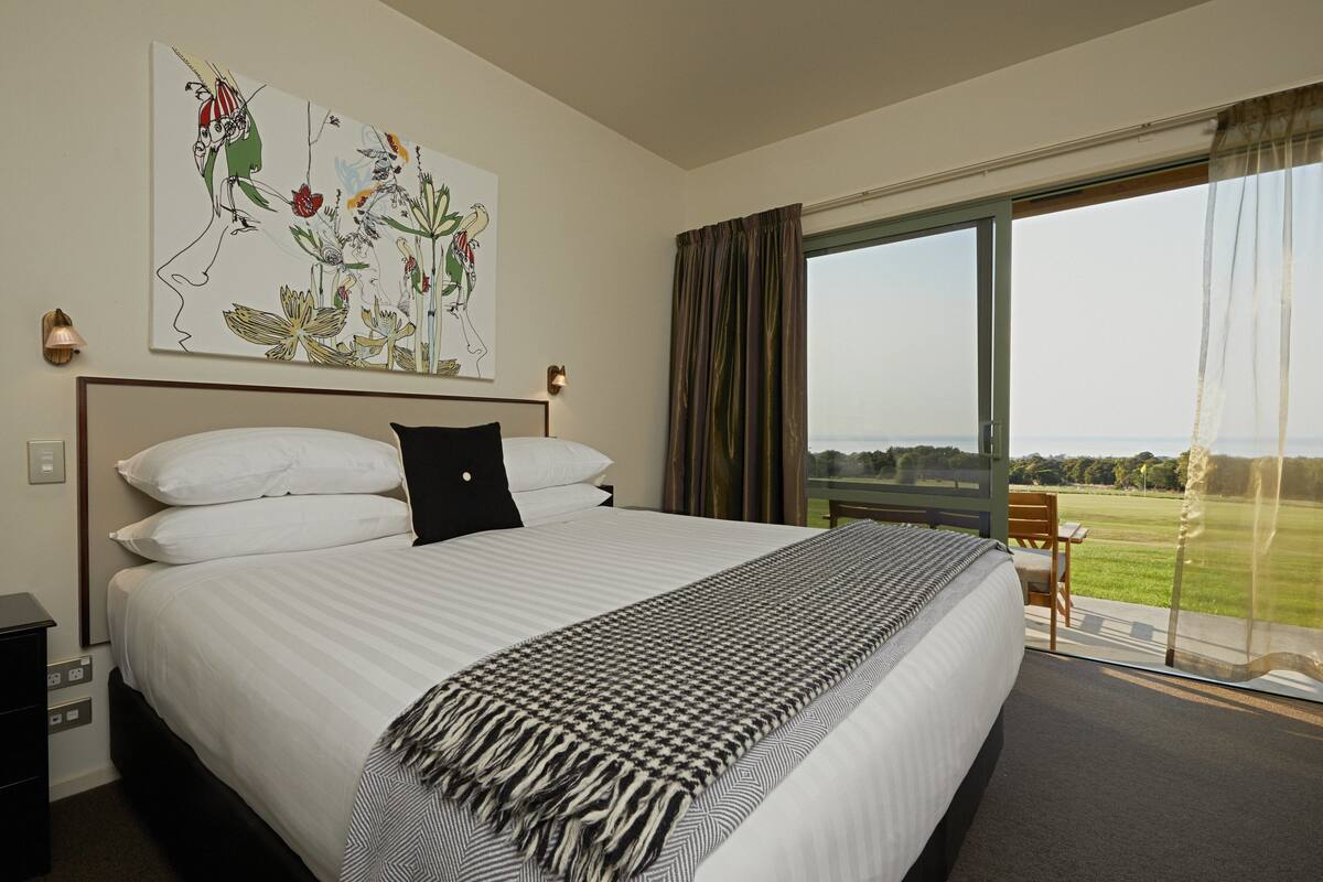 A hotel room with a large bed, a view of the outdoors, and a painting on the wall.