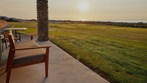 A patio with a stone pillar, a wooden bench, and a table overlooking a grassy field with a view of the horizon. - Koura Bay Resort (Hapuku)