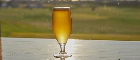 Una cerveza en una mesa de madera con una vista borrosa del exterior al fondo.
