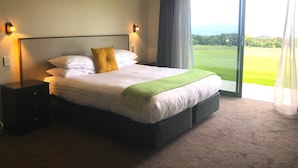 A hotel room with a large bed, two bedside tables, a view of a golf course through the window, and a green throw blanket. - Koura Bay Resort (Hapuku)