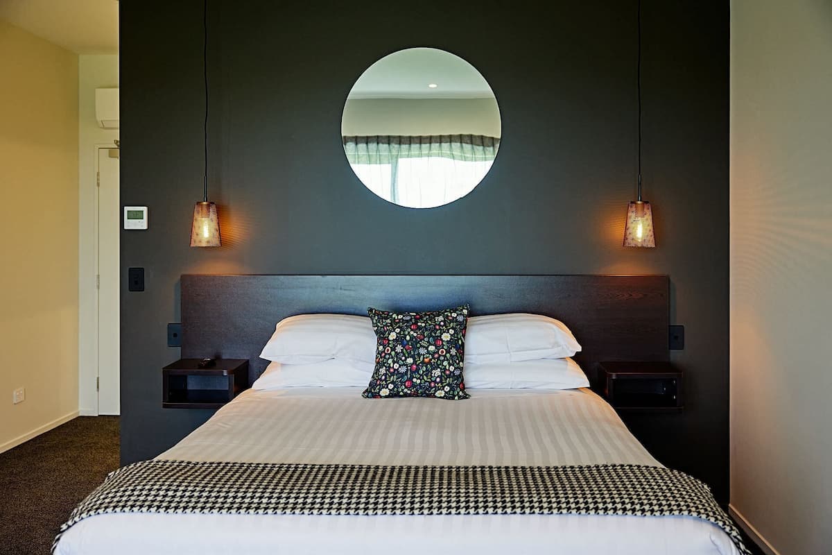 A hotel room with a large bed, two bedside tables, a round mirror above the bed, and two wall-mounted lamps.