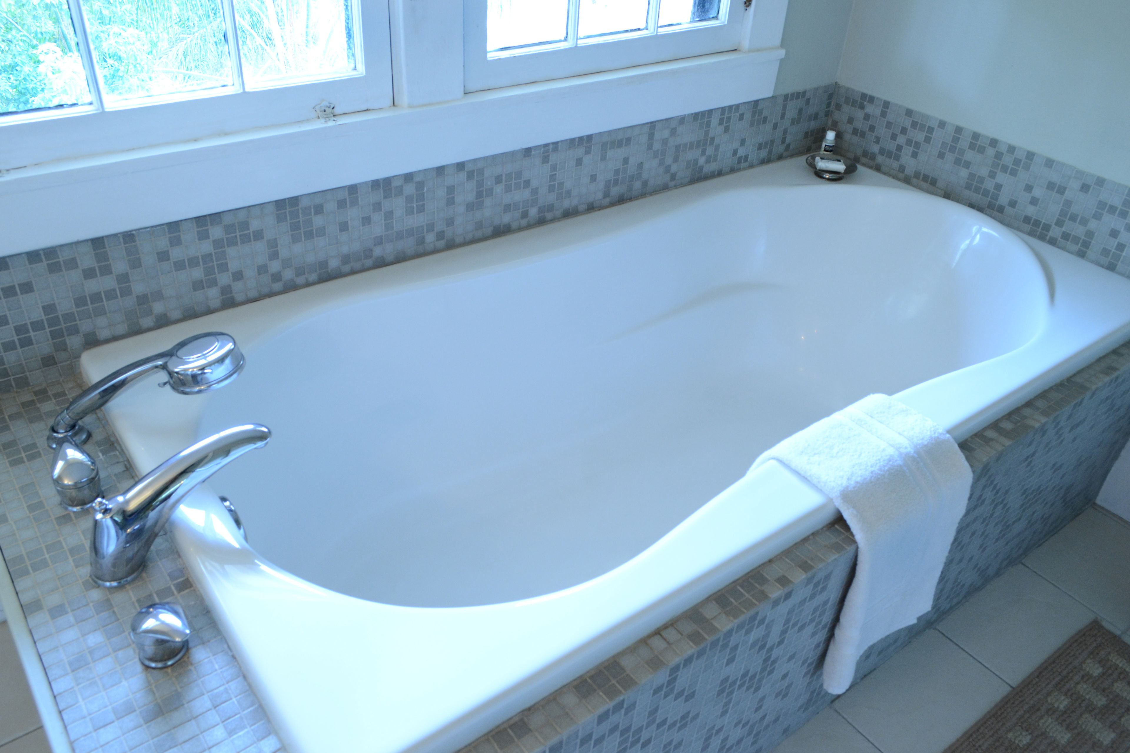 A large, white bathtub with chrome fixtures in a bathroom with tiled walls and a window above.