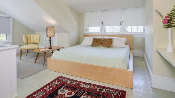 A bedroom with a bed, a chair, a table, and a window. - Adora Inn (Mount Dora)