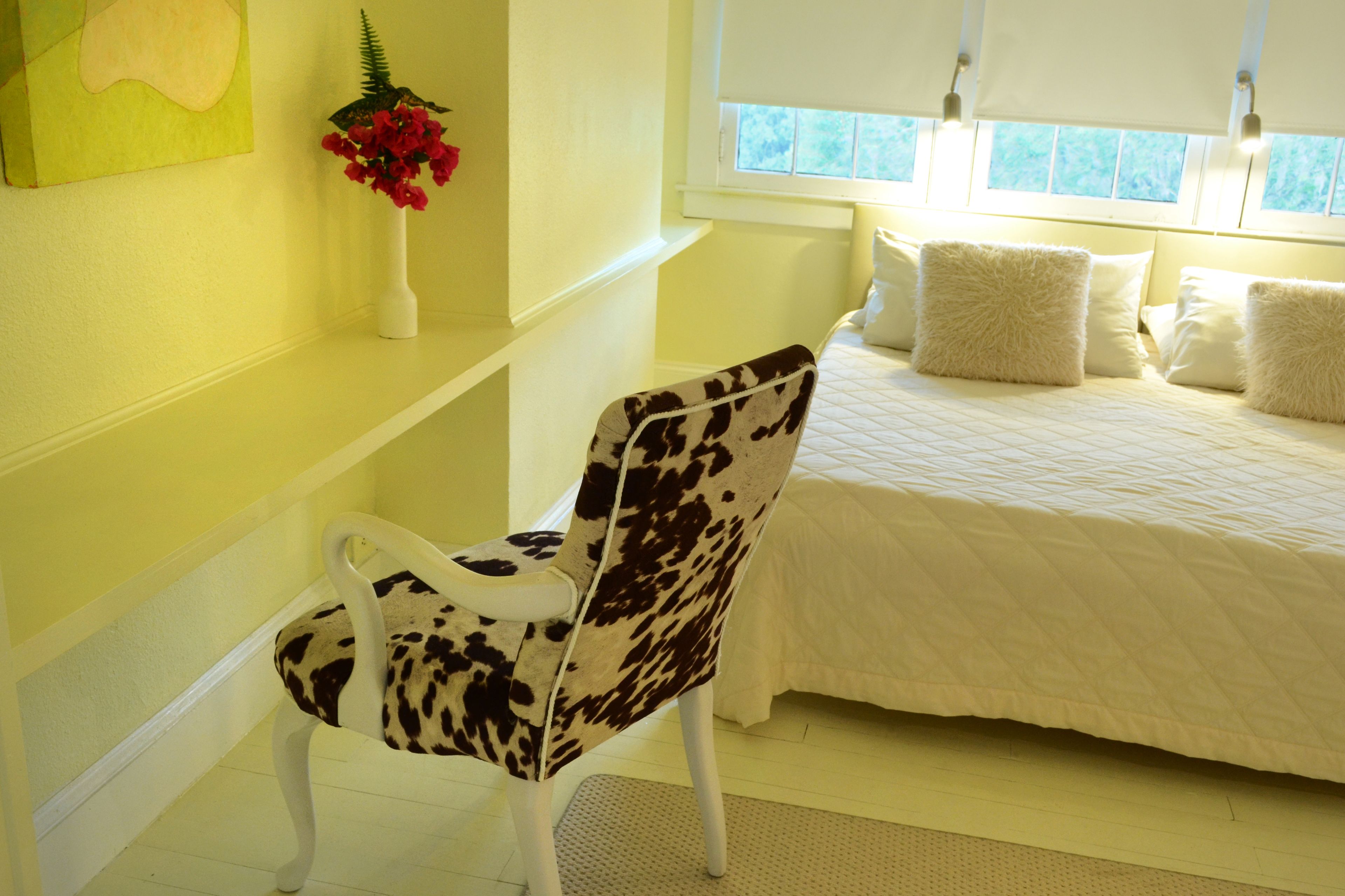 Um quarto com uma cama, uma cadeira, uma janela e um quadro na parede.