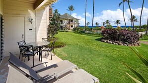 A covered patio with a table and chairs, a lawn, and a view of a house and palm trees.