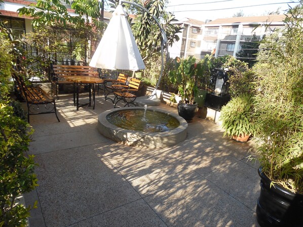 Relax in a serene outdoor space surrounded by lush greenery and a soothing fountain.