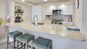 A kitchen with a central island, bar stools, a microwave, and a coffee maker.