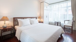 Ein Hotelzimmer mit einem großen Bett, zwei Nachttischen mit Lampen, einem Sessel und einem großen Fenster mit Vorhängen.