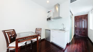 Una cocina compacta con gabinetes blancos, microondas y lavavajillas. Hay una mesa de madera con dos sillas.